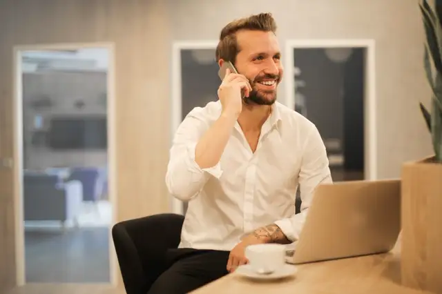 Stock photograph: a person on a mobile phone at a desk with a laptop. Not a customer, not a live receptionist.